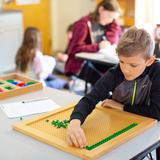 Greensboro Montessori School Photo #2 - Our Upper Elementary program serves fourth, fifth, and sixth graders. Students use tactile learning materials to acquire knowledge. This fourth grader is learning the square root, the lowest common multiple, and factors of a number.