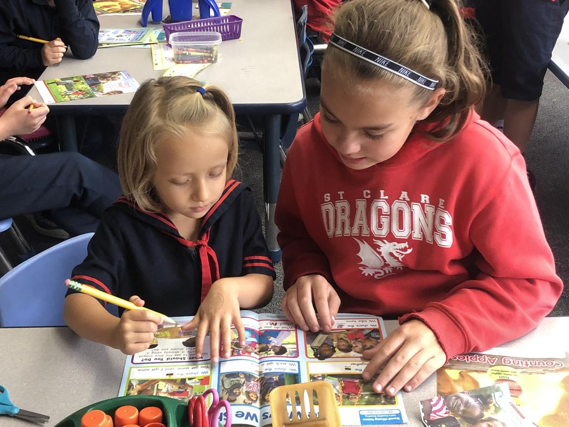St. Clare School Photo #1 - A Kindergarten student reads with her 5th grade buddy. Our buddy program allows students of all ages to learn from each other, grow together, and unleash one another''s potential. All students have a buddy. Our buddy classes are as follows: grades K/5, 1/6, 2/7, 3/8, & 4/Preschool.