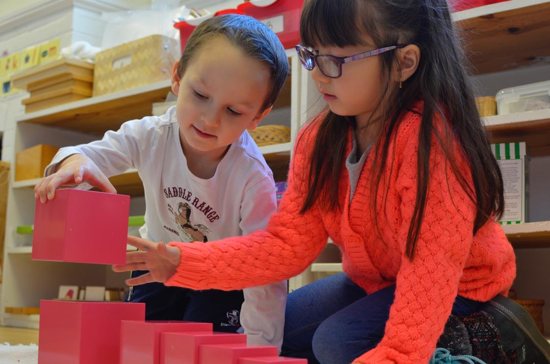 The Gladwyne Montessori School Photo #1 - 3rd year primary student gives a lesson to a 2nd year primary student using the iconic pink tower, specifically designed for children to learn about space, size, and comparison in a concrete manner.