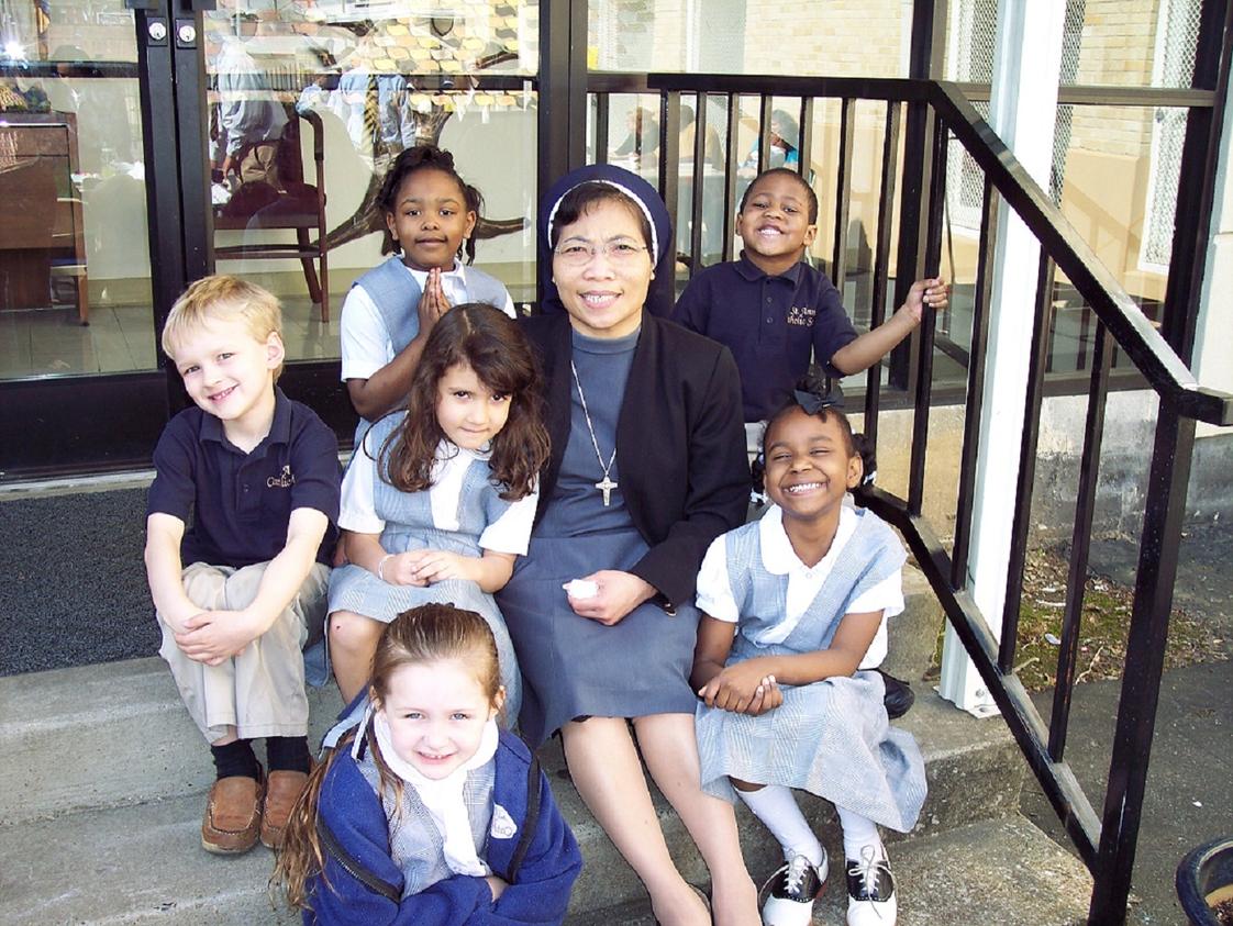 St. Anne Elementary School Photo #1 - Preschool students sit on the steps with Sr. Ancilia Indrati while other students play at recess.