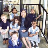 St. Anne Elementary School Photo - Preschool students sit on the steps with Sr. Ancilia Indrati while other students play at recess.