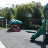 Farmington KinderCare Photo #10 - This playground is utilized by our Toddler Classrooms and our Older Infants. On this playground there are two climbing structures with a cushioned padding underneath. There are also push toys with a sidewalk path. Shade is available to the children underneath the canopy where you will also find picnic tables for the children to sit.